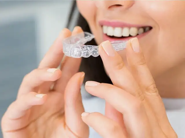 A smiling woman holding a clear aligner tray up to her mouth