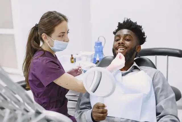 A man holding a hand mirror while a dentist checks his teeth