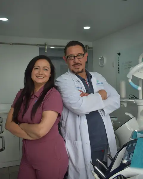 A dentist in a white coat and an assistant in plum scrubs standing in a treatment room