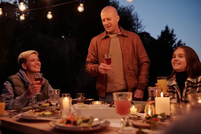 A man raising a glass at an outdoor dinner table with family at dusk